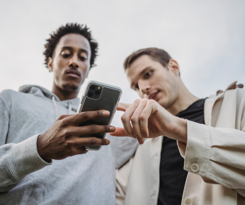 Two men looking at a smartphone, discussing content on the screen.