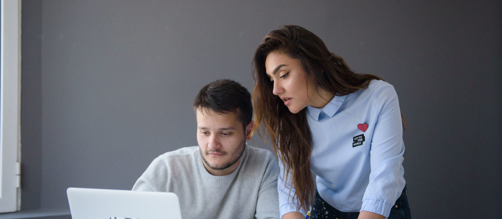 A man and woman sitting at a table with laptops, engaged in work or collaboration.