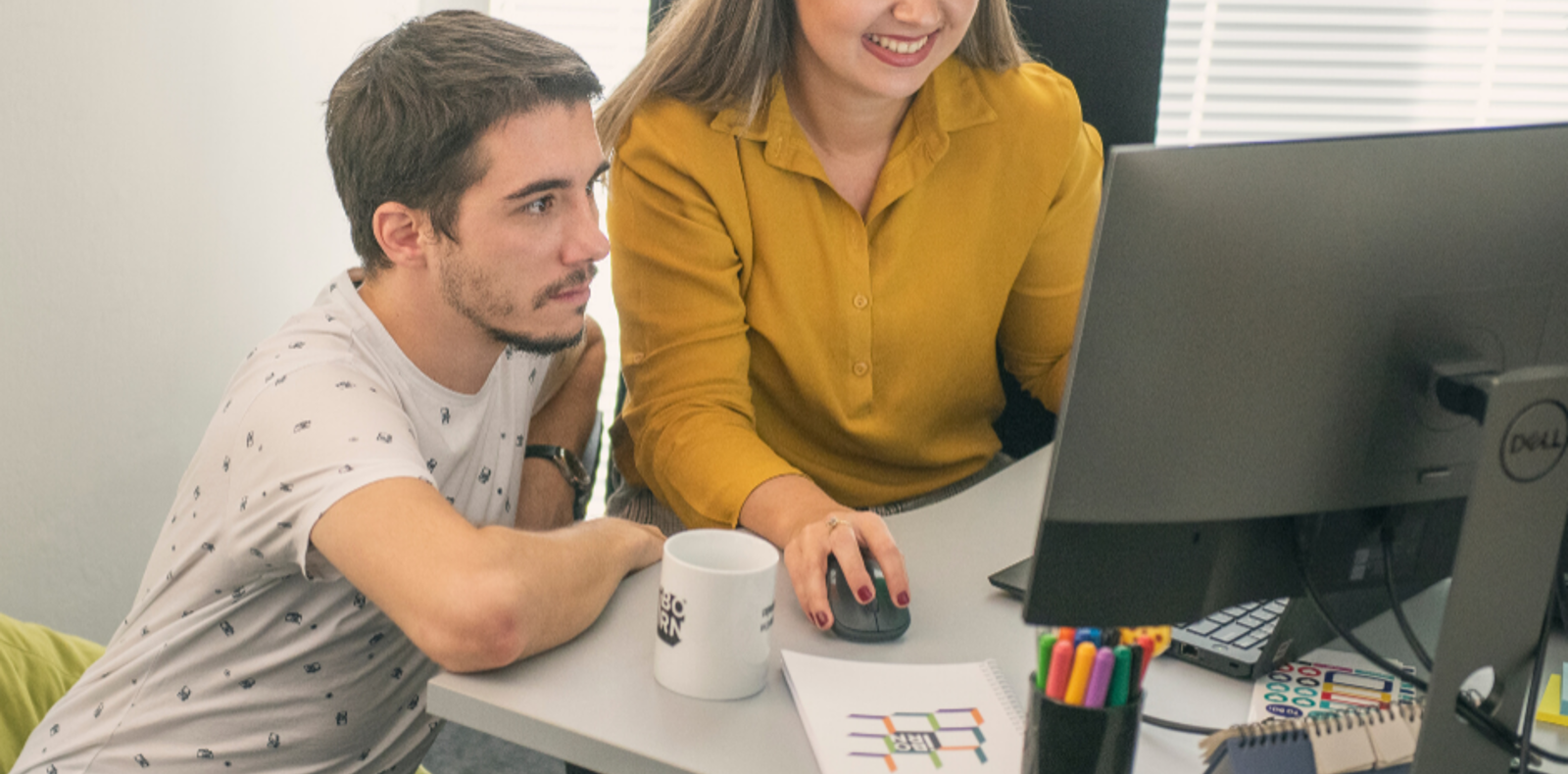 A man and woman sitting at a desk, engaged in conversation and working together on a project.