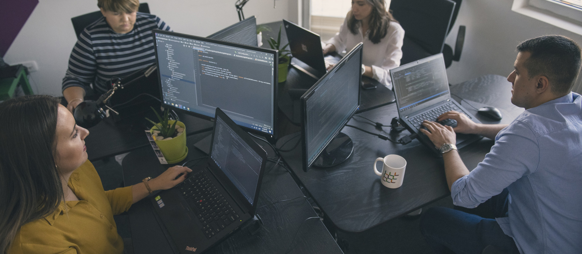 Software engineers sitting at desks, focused on their computer screens in a busy workspace.