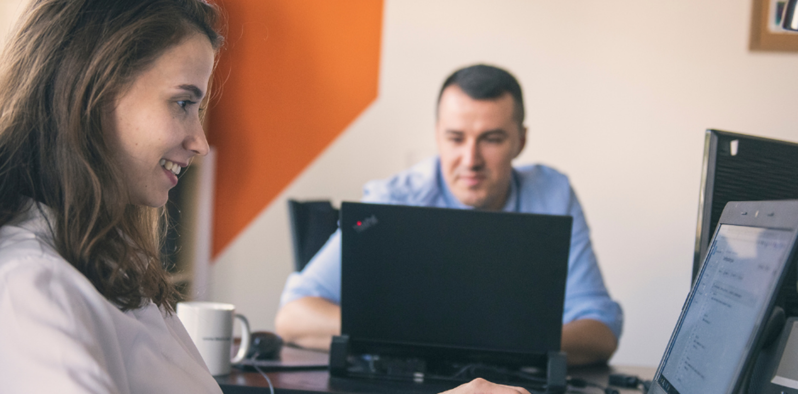 A professional woman and man using a laptop together in an office.