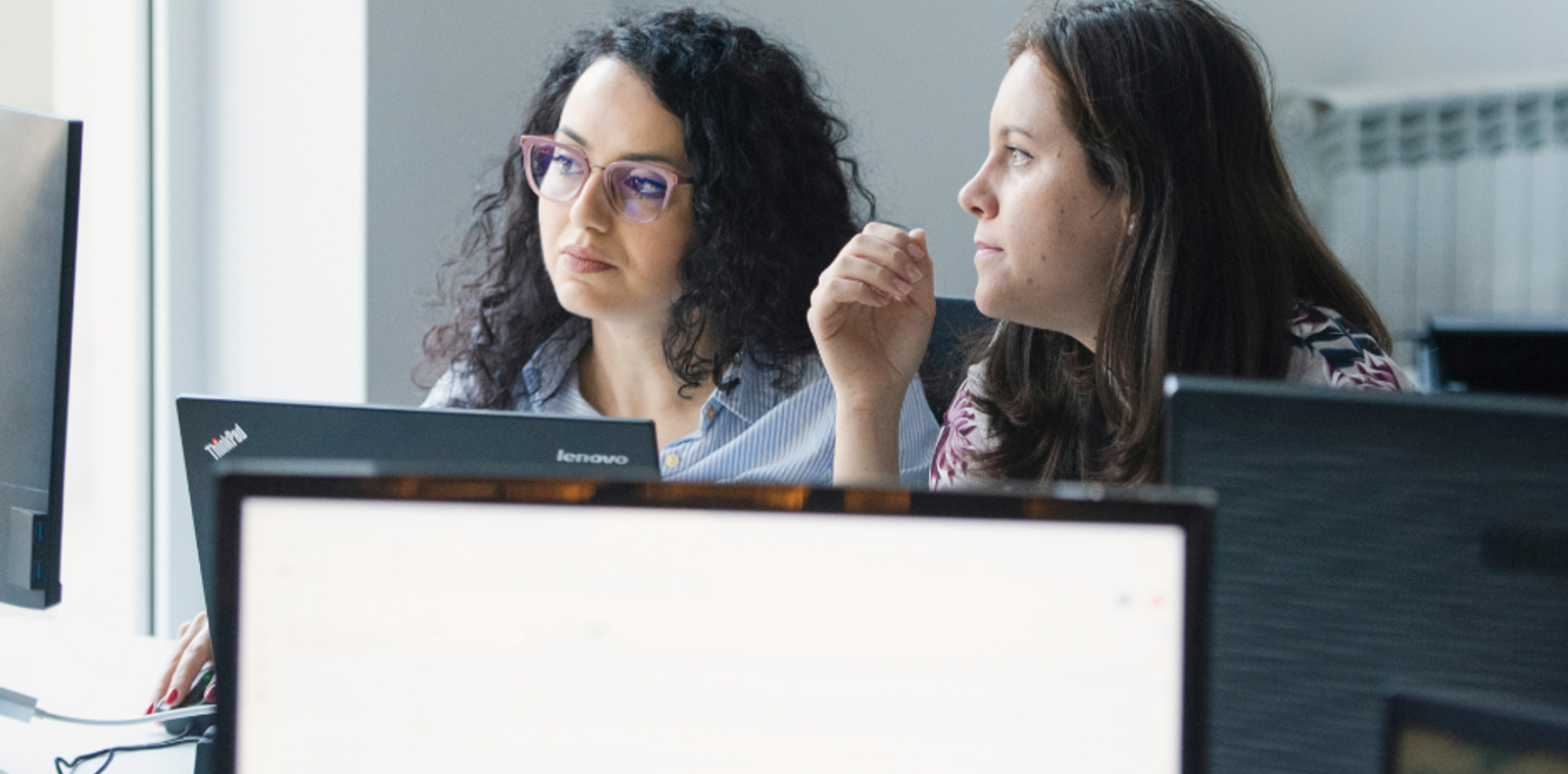 Two women at a desk, engrossed in the content on a computer screen.