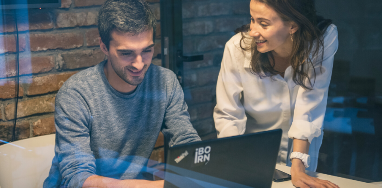 A man and woman collaborating on a laptop in a professional office setting.