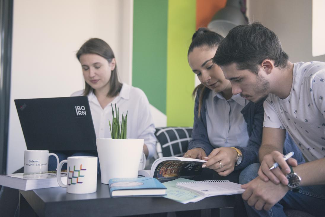 Three individuals sitting at a table, working on a laptop.