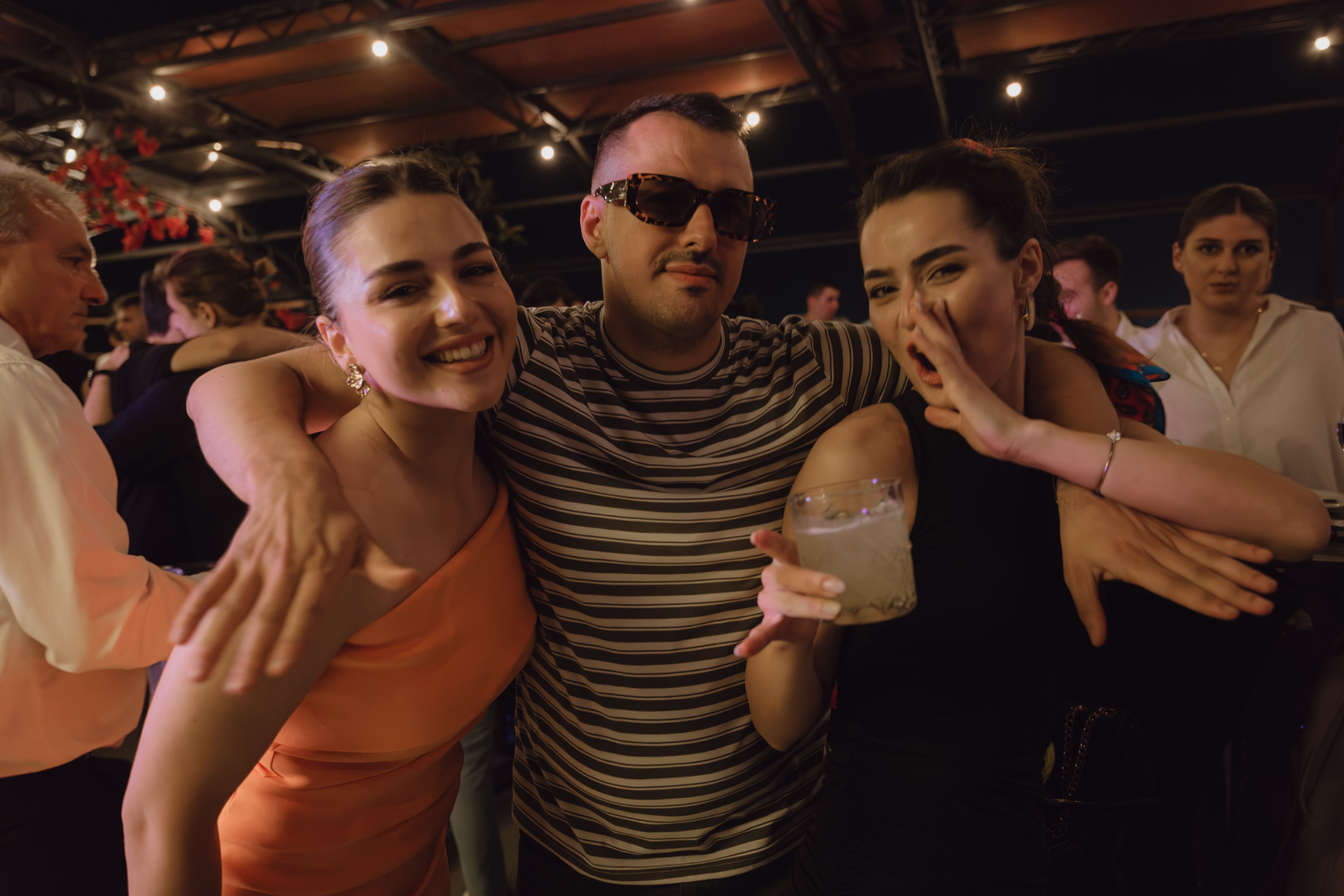 Two women and a man smiling for a photo at a lively party, capturing the joyous atmosphere.