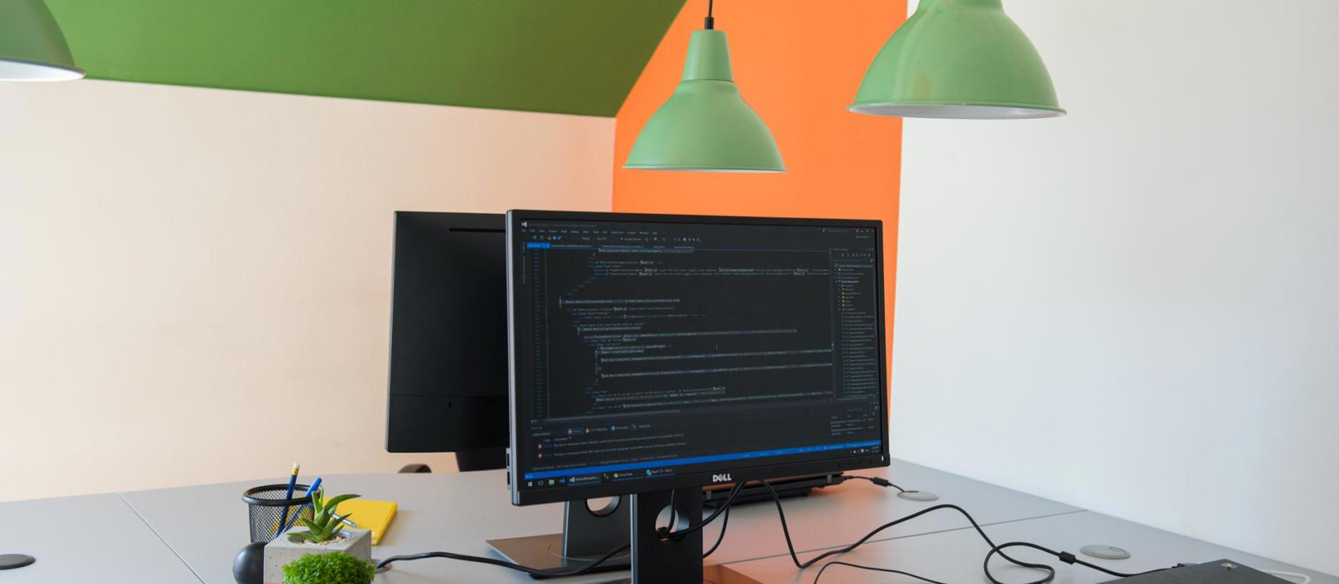 Close-up of computer and laptop screens with people working in the background.