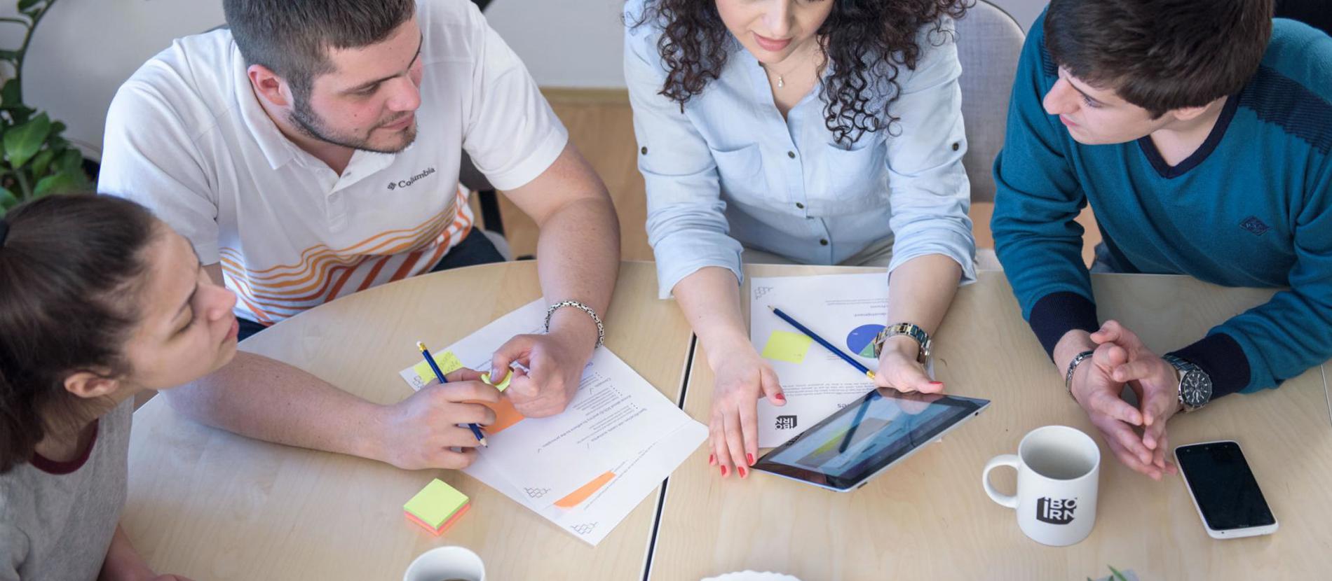 Group of three people gathered around a laptop on a table.