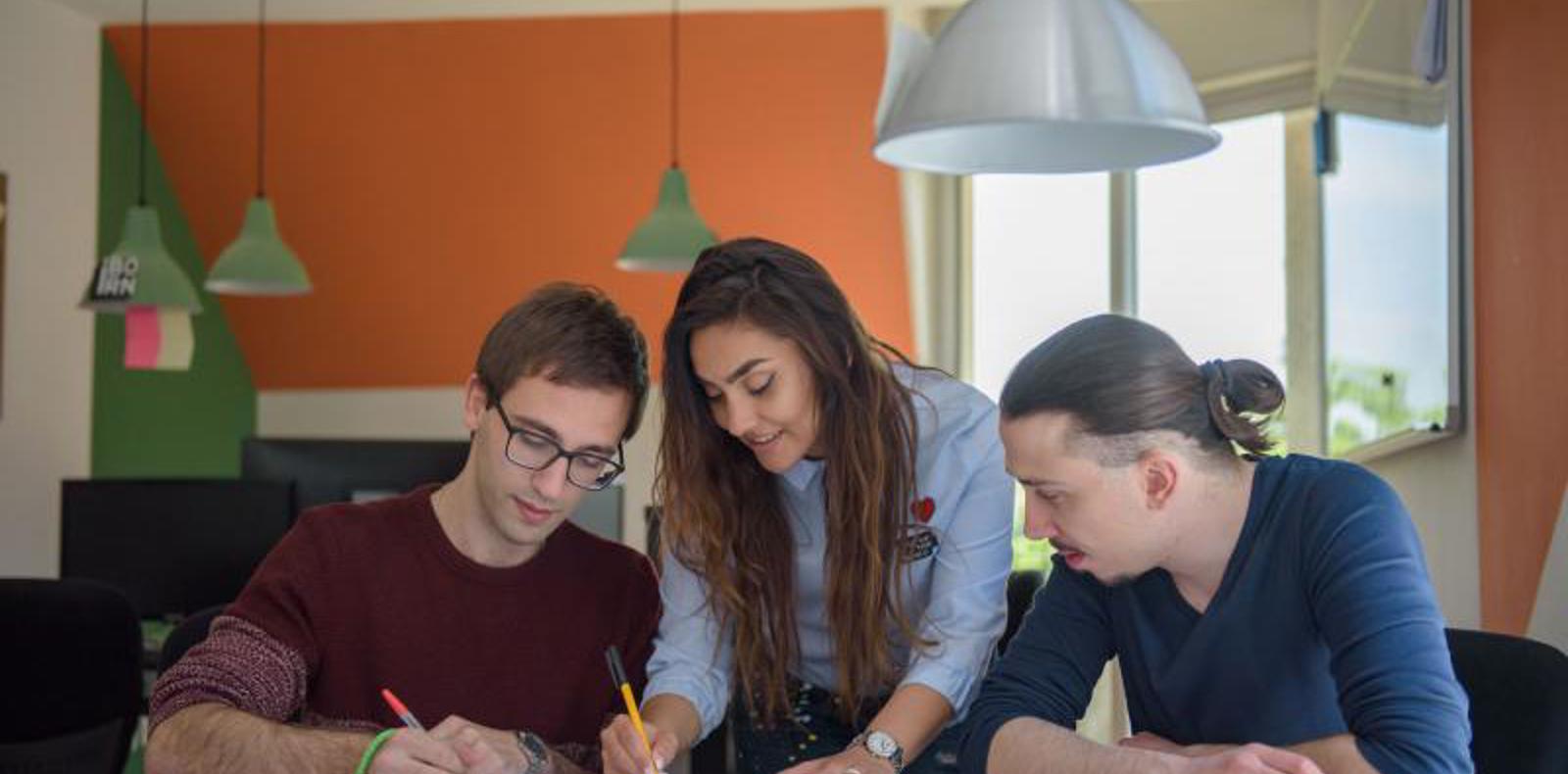 Three people collaborating on a project at a table, brainstorming ideas and working together.