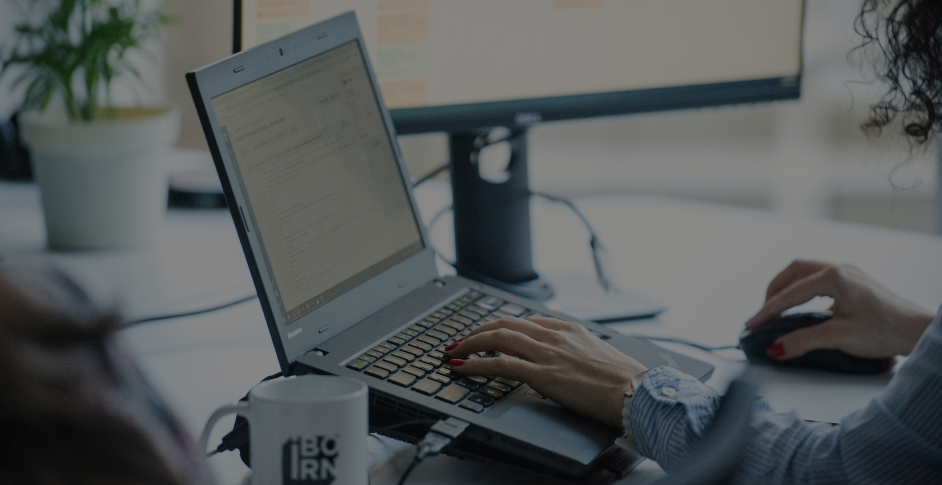 Close-up of hands typing on laptop keyboard, and a mouse and coffee cup with the IBORN logo visible.