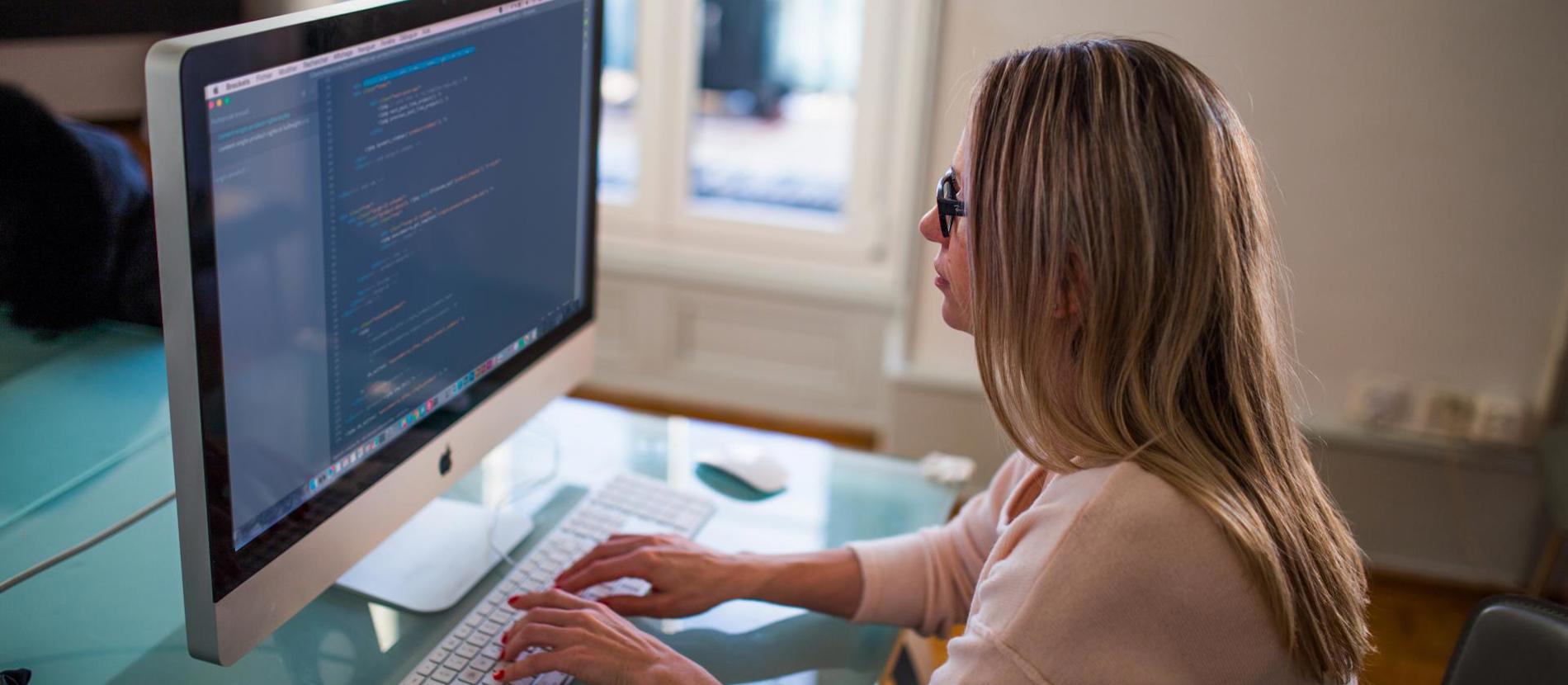 Close-up of computer and laptop screens with people working in the background.