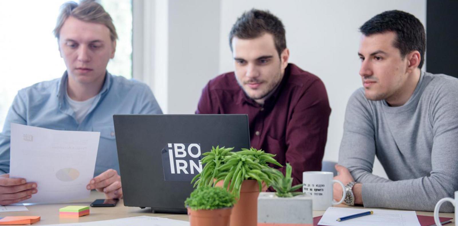 Three men sitting at a table, engrossed in their work on a laptop.