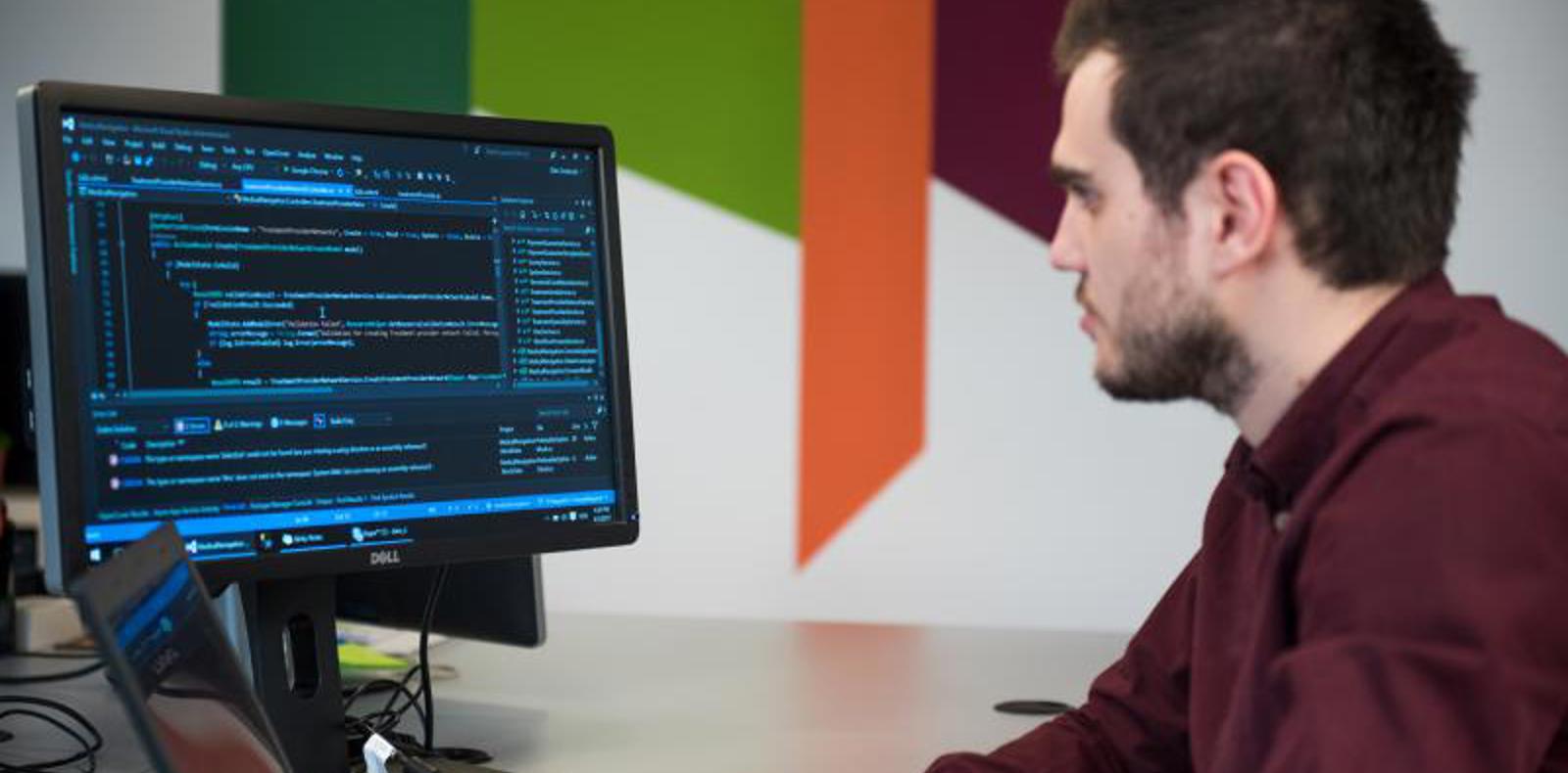 A man working at a desk with a computer and a laptop.