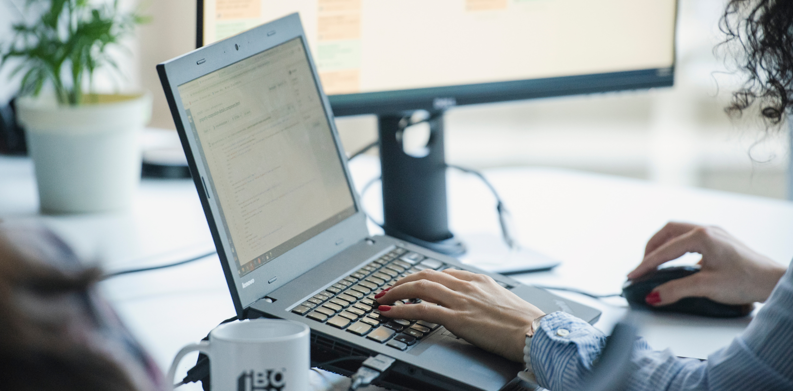 Close-up of hands typing on laptop keyboard, and a mouse and coffee cup with the IBORN logo visible.