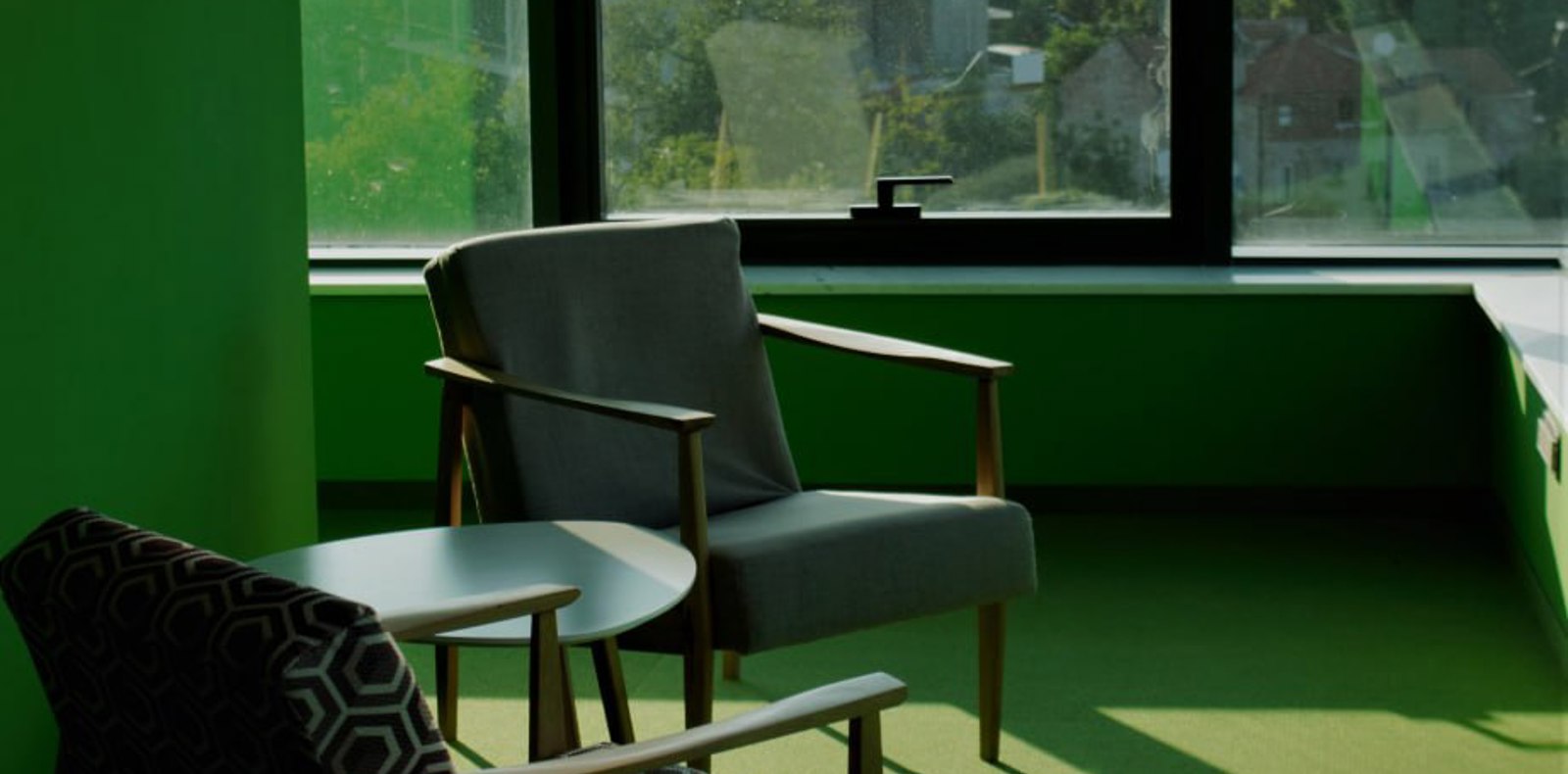 A cozy setup with chairs and table by a window, surrounded by green walls. Perfect enjoy the view while having an individual work or 1:1 meeting.