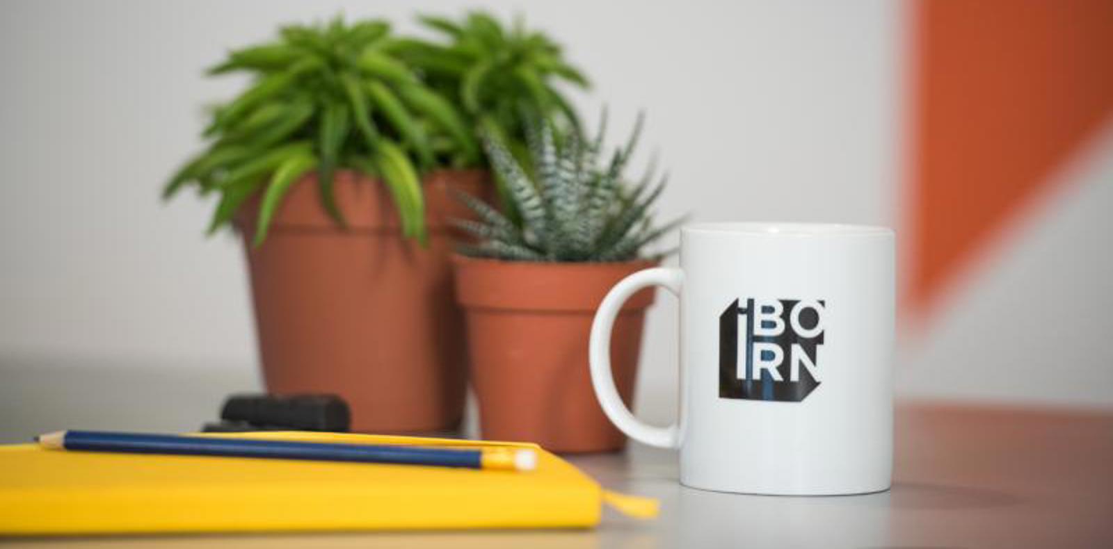 A coffee mug sits on a table alongside a notebook and a plant, creating a cozy and productive atmosphere.