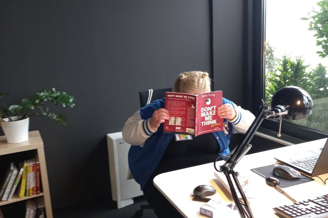 A girl hiding behind a book with a title Don't make me think.