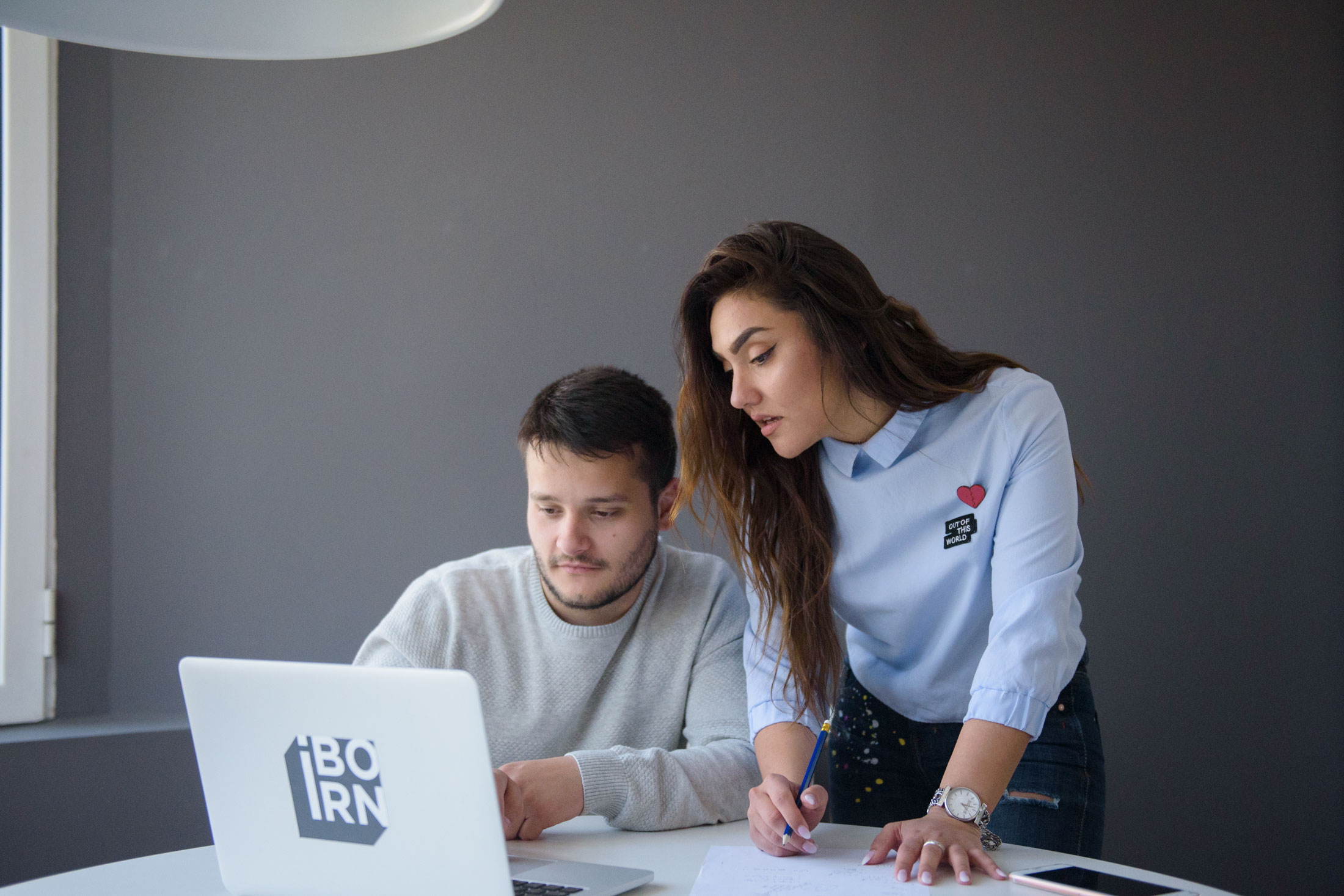 A man and woman sitting together, looking at a laptop screen with focused expressions.