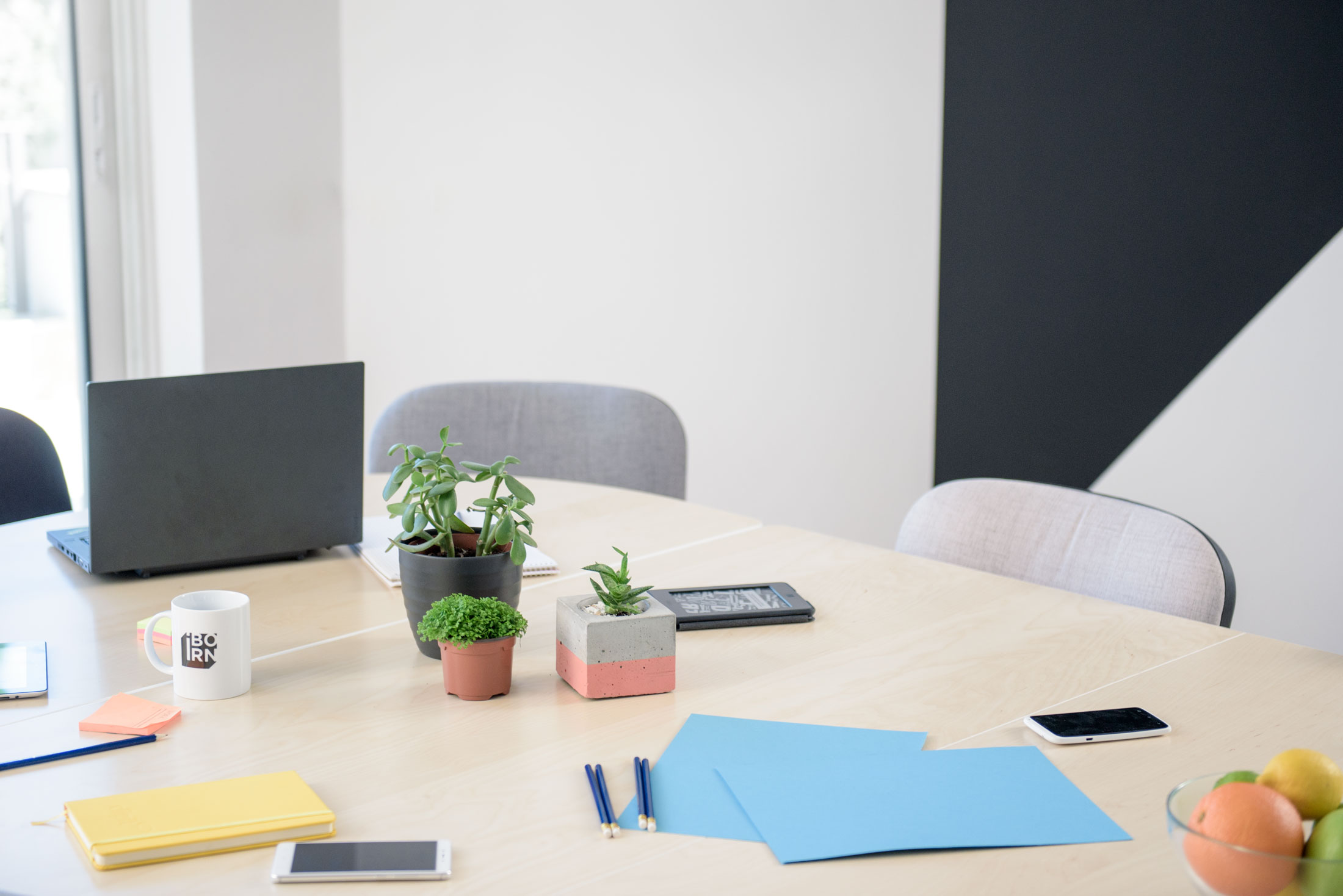 A modern workspace with a laptop, phone, and a touch of nature from a potted plant on a table.