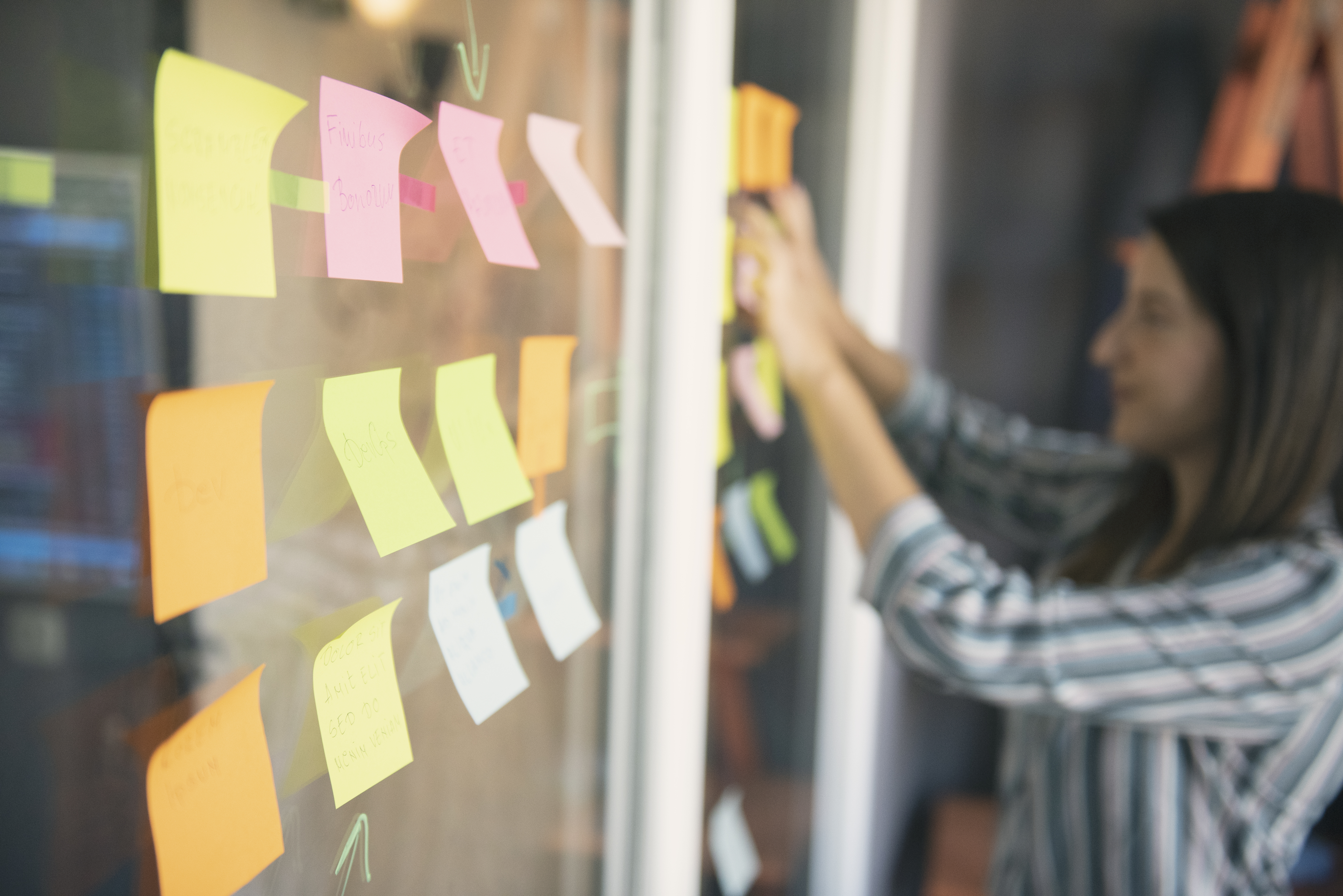 Woman sticking notes on a wall, organizing her thoughts and tasks in a creative way.