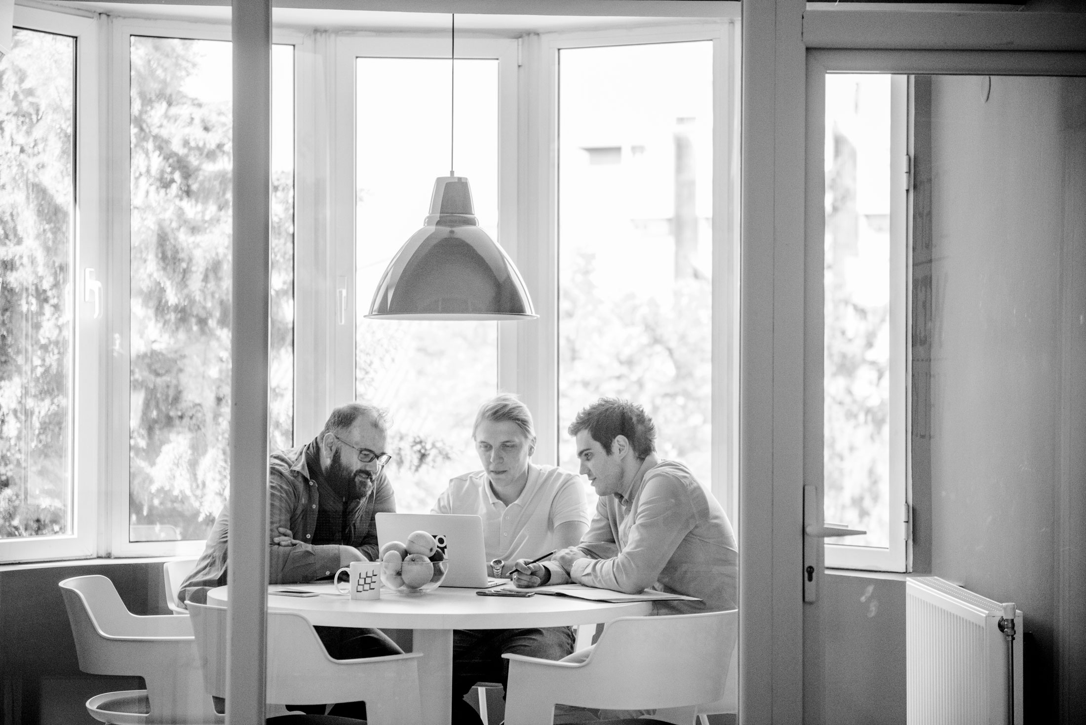 Group of three people gathered around a laptop on a table.