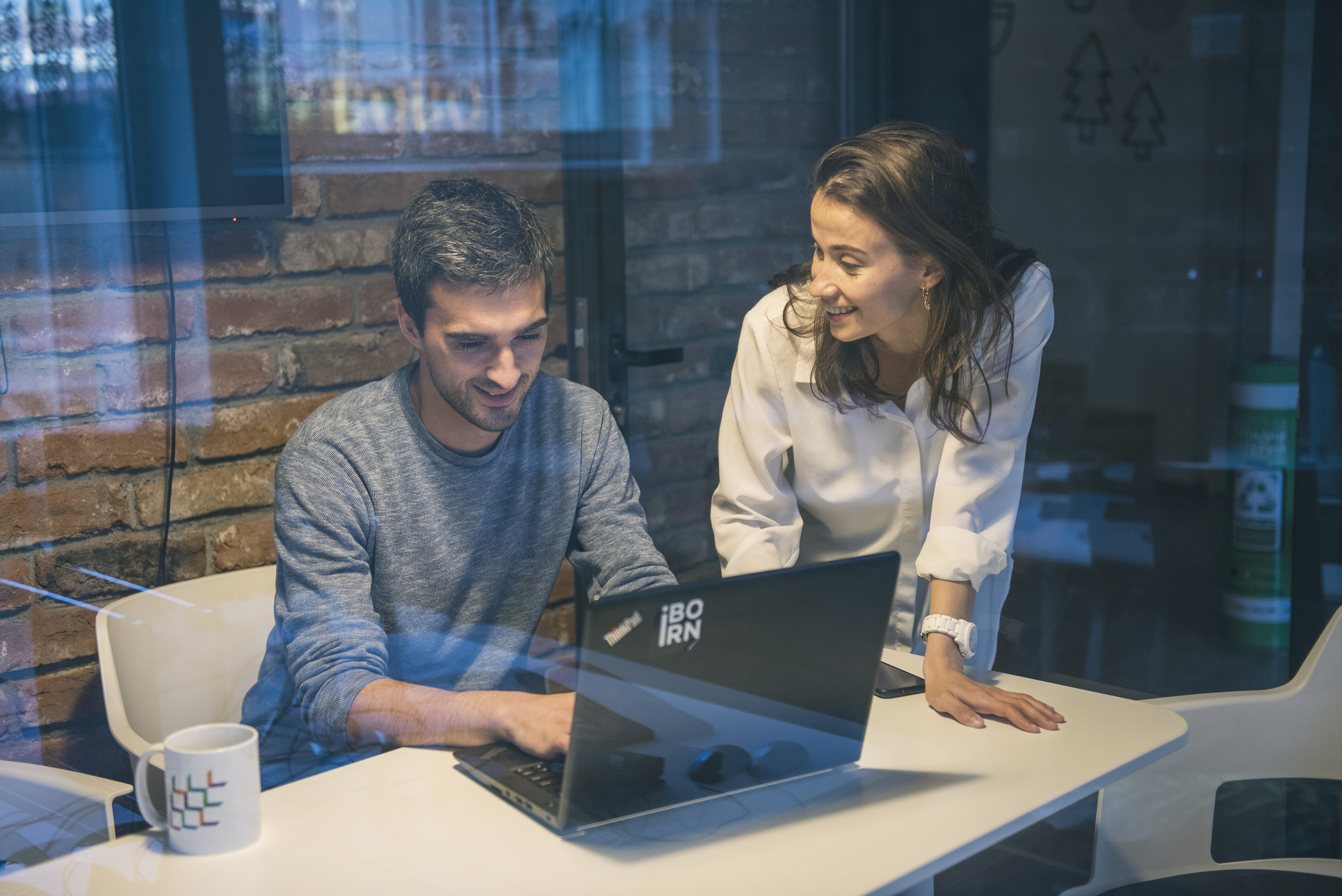 Two colleagues working on a laptop in a modern office environment. 