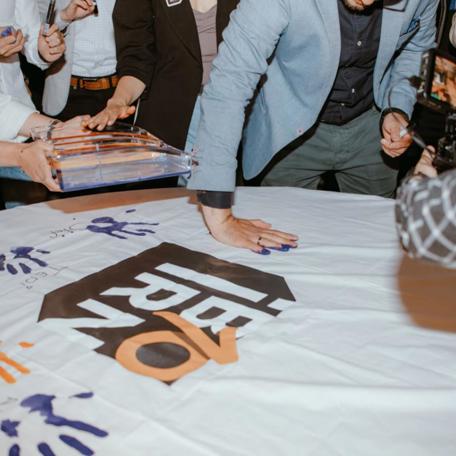 Employees at IBORN.NET gathered around, adding their signatures to a big canvas, symbolizing the mark they left at the company, the teamwork, and shared goals.