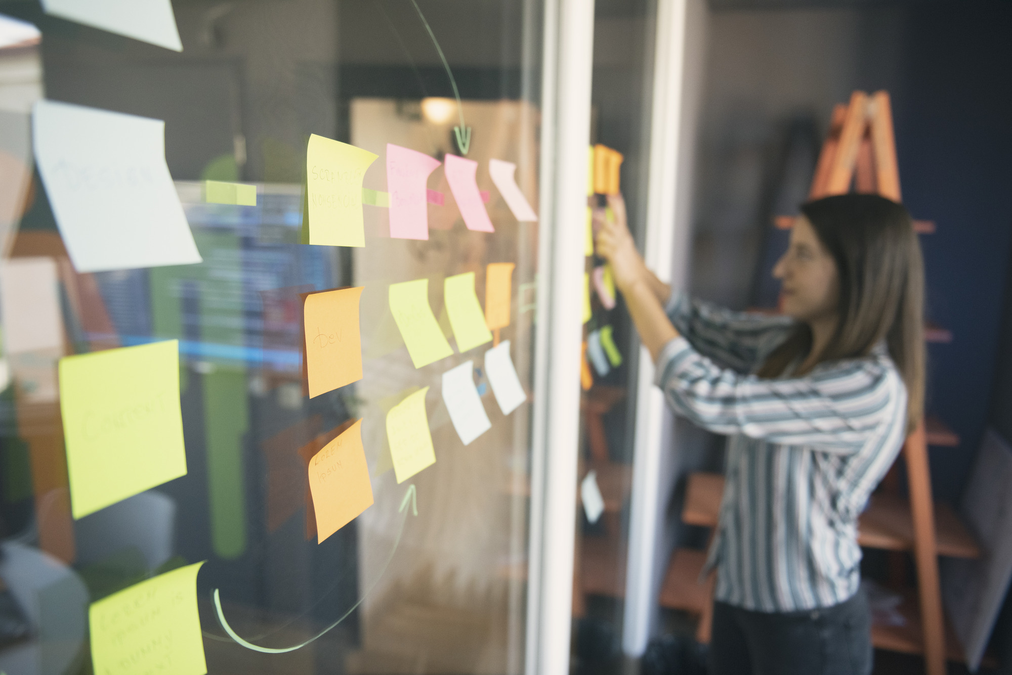 A woman focused on writing post-it notes, planning must-have features for a MVP mobile app. 
