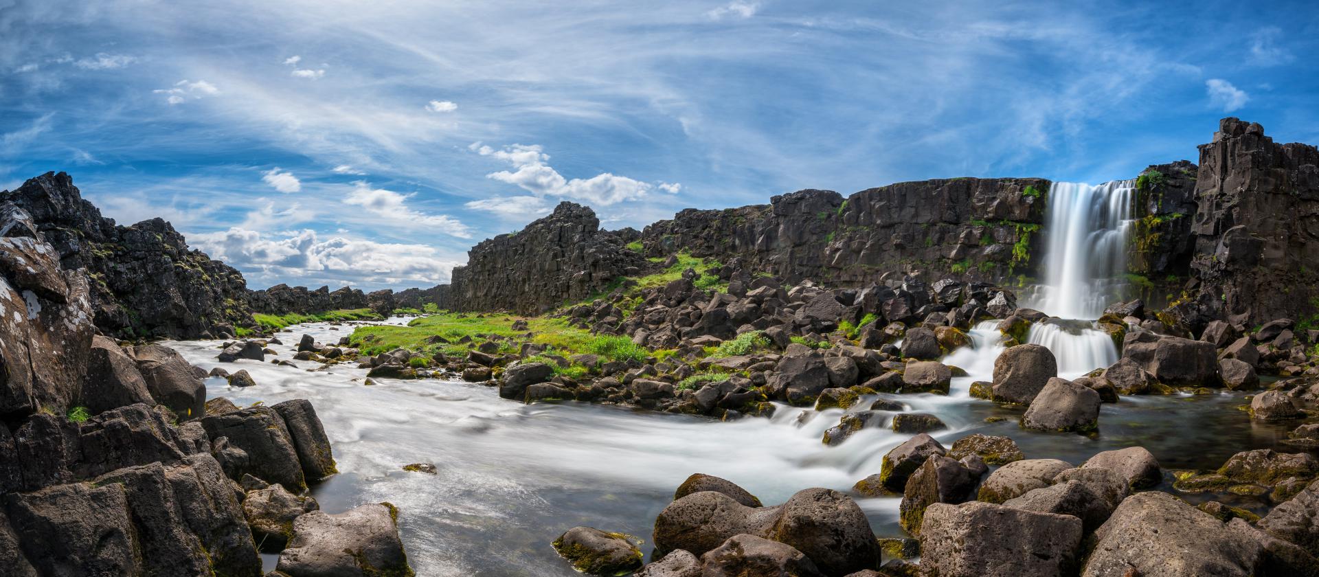 A serene waterfall cascades through a rocky river in a field, creating a picturesque scene of natural beauty.
